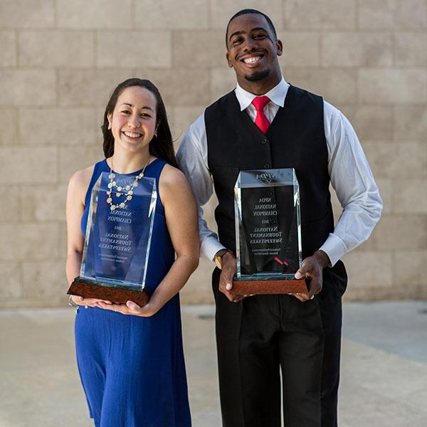 Male and female student holding forensics trophies